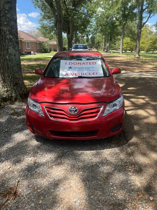 A red sedan with an 'I donated a vehicle' sign on the windshield