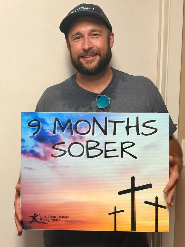 A man holding a sign that reads nine months sober